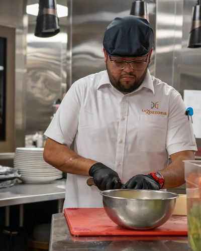 Person in a kitchen wearing a white shirt with 'La Rozzona' logo, preparing food.