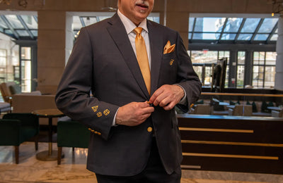 Man in a dark suit with gold accents adjusting his jacket in an indoor setting.