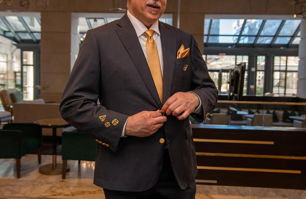 Man in a dark suit with gold accents adjusting his jacket in an indoor setting.